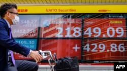 A cyclist wearing a face mask rides past an electric quotation board displaying the morning numbers of the Nikkei 225 Index on the Tokyo Stock Exchange in Tokyo on May 28, 2020. 