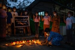 A woman lights a candle while others flash the three-fingered sign of resistance during a candlelight vigil to remember those who died in the military junta's violent response to anti-coup demonstrations in Yangon, Myanmar, April 16, 2021.