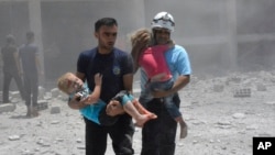 FILE - This photo provided by the Syrian civil defense group known as the White Helmets shows civil defense workers carrying children after airstrikes hit a school housing a number of displaced people, in the western part of Daraa province, Syria, June 14, 2017.