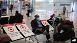 A man sits wearing a face shield in the arrivals area at Heathrow Airpot in London, June 8, 2020, on the first day of new rules for the people arriving in Britain from overseas.