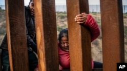  FILE - A migrant climbs the border fence before jumping into the U.S. in San Diego, California, from Tijuana, Mexico, Dec. 27, 2018. 
