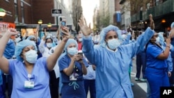 FILE - Nurses and medical workers react as police officers and pedestrians cheer them outside Lenox Hill Hospital Wednesday, April 15, 2020, in New York.