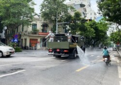 Men wearing personal protective equipment (PPE) disinfect a street as the city is under lockdown during the COVID-19 outbreak in Hanoi, Vietnam July 26, 2021.