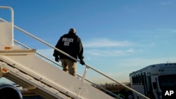 FILE - In this Nov. 16, 2018, photo, an officer watches as immigrants who entered the United States illegally are deported on a flight to El Salvador by U.S. Immigration and Customs Enforcement in Houston.