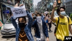 បាតុករ​ម្នាក់កាន់​ស្លាកសញ្ញា​គាំទ្រ​រដ្ឋាភិបាល​រួបរួម​ជាតិ ខណៈ​ដែល​អ្នក​ខ្លះ​ទៀត​លើក​ម្រាម​ដៃ​បី​ជា​សញ្ញា​គាំទ្រ​ដល់​ការ​តវ៉ា​ប្រឆាំង​នឹង​រដ្ឋាភិបាល​យោធា​​ ទីក្រុង​រ៉ង់ហ្គូន ប្រទេស​មីយ៉ាន់ម៉ា ថ្ងៃទី២៧ ខែមេសា ឆ្នាំ២០២១។