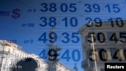 Papan bertuliskan nilai-nilai pertukaran woman is reflected in a window with a board displaying currency exchange rates in St. Petersburg, Russia, Sept. 16, 2014. 
