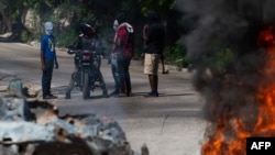 As bodies of alleged gang members burn in the foreground, local residents speak with a motorist in the street in Petion-Ville, a suburb of Port-au-Prince, Haiti, Nov. 19, 2024.