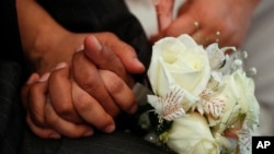 FILE - Newlyweds hold hands during a mass wedding ceremony.