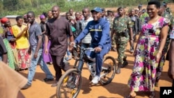 President Pierre Nkurunziza arrives riding a bicycle, accompanied by first lady Denise Bucumi Nkurunziza, right, to cast his vote for the presidential election, in Ngozi, Burundi, July 21, 2015.