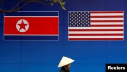 Seseorang berjalan melewati spanduk bendera Korea Utara dan AS di depan bendera Korea Utara-AS. KTT di Hanoi, Vietnam, 25 Februari 2019. (Foto: Reuters)