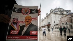FILE - A man holds a poster, with images of Saudi Crown Prince Mohammed bin Salman and journalist Jamal Khashoggi, that describes the prince as an “assassin” and Khashoggi as a “martyr” during funeral prayers in absentia for Khashoggi.