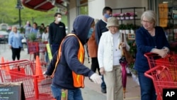 Doorman Dilon Moore, center, helps with shopping carts and controls the number of customers allowed to shop at one time at a Trader Joe's supermarket in Omaha, Neb., May 7, 2020. 