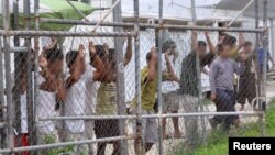 FILE - Asylum-seekers look through a fence at the Manus Island detention center in Papua New Guinea, March 21, 2014. 