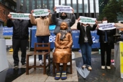 FILE - Protesters hold banners during a rally to mark the March First Independence Movement Day against Japanese colonial rule, in front of a statue symbolizing a wartime sex slave, near Japan's embassy in Seoul, South Korea, March 1, 2021.