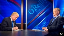 Republican presidential candidate Donald Trump, left, signs his book for Bill O'Reilly, right, during his appearance on Fox's news talk show "The O'Reilly Factor," Nov. 6, 2015, in New York.