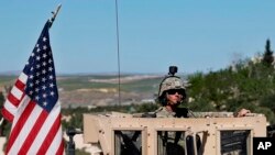 FILE - A U.S. soldier sits in his armored vehicle on a road leading to the tense front line in Manbij, Syria, April 4, 2018.