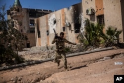 FILE - A fighter of the Libyan forces, affiliated with the Tripoli government, runs for cover while fighting against Islamic State positions in Sirte, Libya, Sept. 22, 2016.