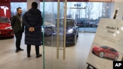 A sales staff chats with a customer at a Tesla store near a poster announcing orders of the Model 3 electric cars in Beijing, China, Monday, Jan. 7, 2019. 