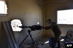 A fighter from the Syrian pro-government forces mans a gun inside damaged houses as they approach the Baeedin district in eastern Aleppo, near Masaken Hanano, November 23, 2016.