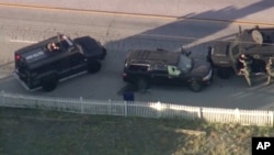 Armored vehicles surround an SUV following a second shootout in which two suspects were killed and a police officer was wounded.