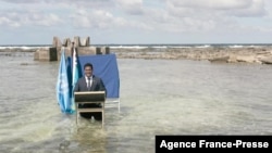 This videograb taken from footage released by the Tuvalu Ministry of Justice, Communications and Foreign Affairs Nov. 9, 2021, shows Foreign Minister Simon Kofe standing thigh-deep in seawater off the coast of Tuvalu, as he addresses the COP26 conference in Glasgow.