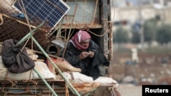 FILE - An internally displaced man who fled from Idlib rolls a cigarette as he rides on a pickup truck with belongings in Azaz, Syria, Feb. 15, 2020.