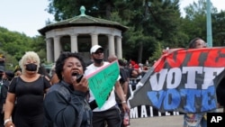 Holding a sign that reads, "The American system is rigged," a woman amplifies her voice as she implores protesters to rise to the occasion and become activists during a Caribbean-led Black Lives Matter rally at Brooklyn's Grand Army Plaza.