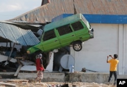 A man takes a photo of a car lifted into the air with his mobile phone following a massive earthquake and tsunami at Talise beach in Palu, Central Sulawesi, Indonesia, Oct. 1, 2018.