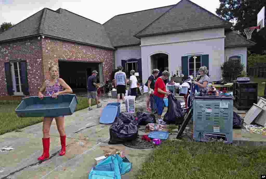 Raven Harelson, 59, left, carries a drawer to the trash heap in front the home of Sheila Siener, 58, as friends and family help to clean out the flood-damaged home in St. Amant, Louisiana, Aug. 20, 2016.