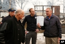 California Gov. Jerry Brown, (2-L), looks at a student work book, held up by Interior Secretary Ryan Zinke, that was found during a tour of the fire-ravaged Paradise Elementary School, Nov. 14, 2018, in Paradise, California.