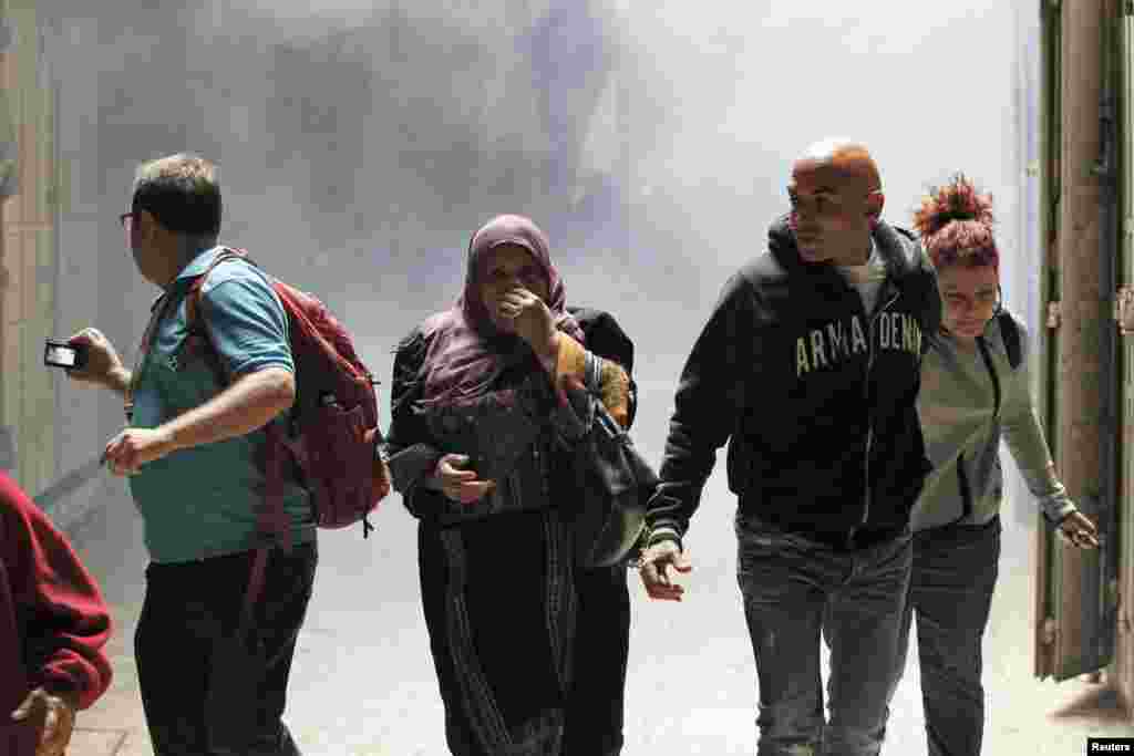 People walk away from tear gas smoke during clashes between Palestinians and Israeli security forces inside the Old City of Jerusalem, Oct. 30, 2014. 