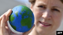 FILE - An environmental militant shows an orange, painted as a globe, during an event to mark the Earth Overshoot Day on Aug. 1, 2018 in Berlin. It marks the date when we (all of humanity) have used more from nature than our planet can renew in the entire year.