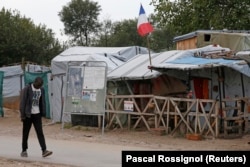 A migrant walks past a shelter with a French flag in the southern area of the camp called the "Jungle" in Calais, France, Sept. 26, 2016.