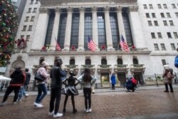 Visitors to the New York Stock Exchange pause to take photos, Jan. 3, 2020, in New York. Stocks fell broadly in midday trading and oil prices surged after U.S. forces in Iraq killed a top Iranian general.