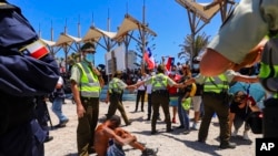 La policía chilena protege a un migrante venezolano que fue atacado por un manifestante que marchaba contra la migración ilegal, en una playa de Iquique, Chile, el domingo 30 de enero de 2022.