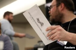 Election volunteer Tyler Jentoft-Johnson holds an absentee ballot as they're counted at City Hall during the presidential primary election held amid the COVID-19 pandemic in Beloit, Wisconsin, on April 7, 2020.