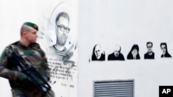 Seorang tentara Perancis berpatroli di dekat lukisan kartunis (dari kiri: Charb, Honore, Wolinski, Cabu, Charb dan Tignous) di luar bekas kantor Charlie Hebdo di Paris, Perancis, setahun pasca serangan di kantor tersebut (Foto: dok).