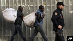 Immigrant street vendors in Spain walk along carrying their goods as police stand guard in Madrid, Spain
