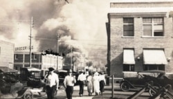 FILE - In this photo provided by McFarlin Library at the University of Tulsa, two armed men walk away from burning buildings as others walk in the opposite direction during the Tulsa Race Massacre, June 1, 1921, in Tulsa, Okla.
