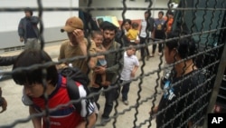 Ethnic Uighur Muslims line up beside a police van in Khlong Hoi Khong of southern Songkhla province, Thailand, Mar. 15, 2014. 