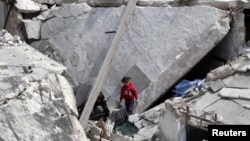 FILE - A Syrian woman cries as her wounded child lies on an operating table following artillery fire on the regime-held city of Aleppo, March 21, 2021.