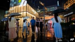 FILE - People walk under the rain with umbrellas at Taikoo Li Sanlitun in Beijing, July, 30, 2024. 