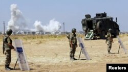 Turkish soldiers stand guard near the Mursitpinar border gate in Sanliurfa province as smoke rises in the Syrian town of Kobani in the background, June 27, 2015.