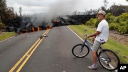 FILE - Hawaii resident Sam Knox watches the lava stretch across the road, Saturday, May 5, 2018, in Pahoa, Hawaii. (AP Photo/Marco Garcia)