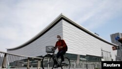 FILE - A man wearing a protective mask amid COVID-19 outbreak cycles past Ariake Arena in Tokyo, Japan, Apr. 8, 2021. 