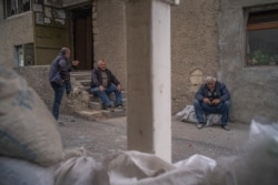 Men sit outside an underground shelter before bombs and sirens go off in Nagorno-Karabakh, Oct. 9, 2020. (Yan Boechat/VOA)
