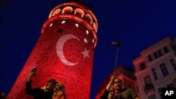 People take photos at the iconic Galata Tower, illuminated in Turkish flag colors, in Istanbul, July 30, 2016. Some signals from President Recep Tayyip Erdogan's administration show no letup in reprisals following an abortive coup attempt two weeks ago.