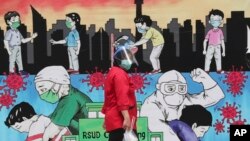 Seorang karyawan melintas di depan mural yang dibuat untuk menghormati tenaga kesehatan di RSUD Cengkareng, Jakarta, Kamis, 24 Juni 2021. 