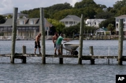 From left, Josh Clappsy, Blake Price, and JB Phillips remove boards from a dock in hopes to save it from rising waters in Swansboro, North Carolina, Sept. 11, 2018.