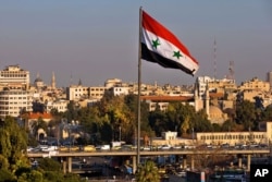 A Syrian national flag waves as vehicles move slowly on a bridge during rush hour, in Damascus, Syria, Feb. 28, 2016.